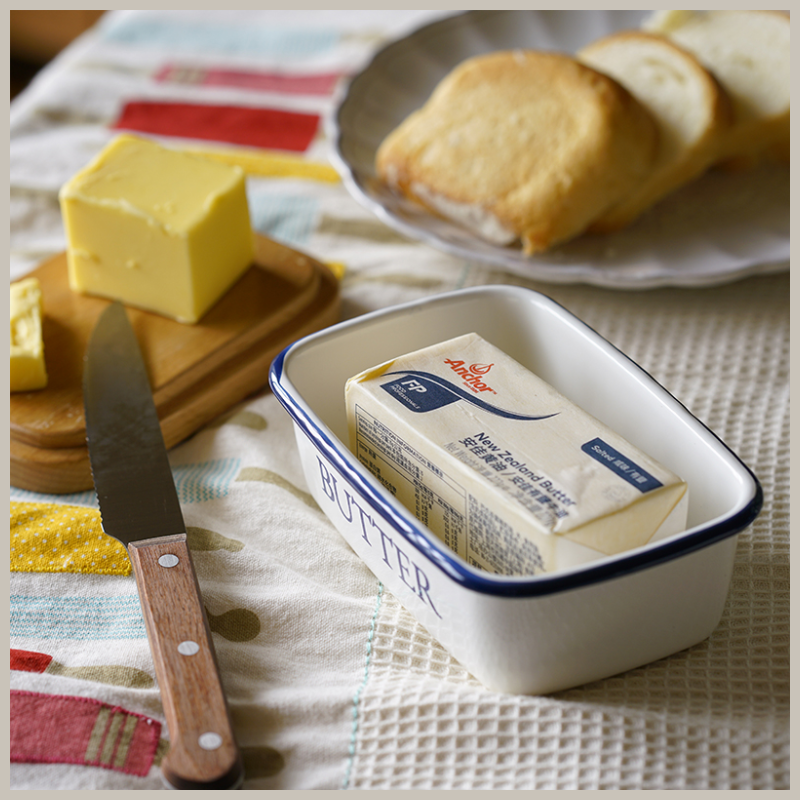 Blue and white Shaker style enamel butter dish. Photo shows open dish on table and filled with large stick of butter. 