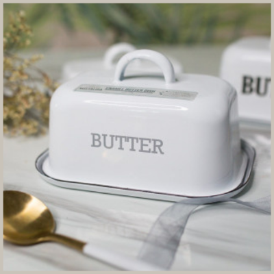 A white enamel butter dish and lid with nostalgic flair. Gray trim around the base. Gray letters across lid spell &quot;butter&quot;, and a loop enamel handle on top. 