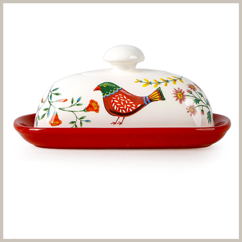  A butter dish with European flair. Glaze pottery with a while lid that has a red colorful bird and a floral design. Sits on a vibrant red base. 