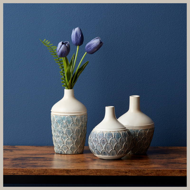 Set of 3 gourd vases with geometric leaf pattern in blue hues on cream. Sitting on a wood table with deep blue wall as background. 