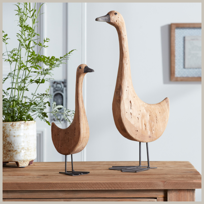 A pair of tall fir wood geese with iron beaks, eyes and legs. Sitting on a wooden table. 