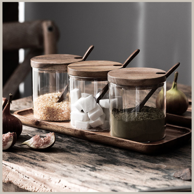 Glass Seasoning Jar Set with three jars, wooden lids, spoons & tray. Set is sitting on a rustic counter. 